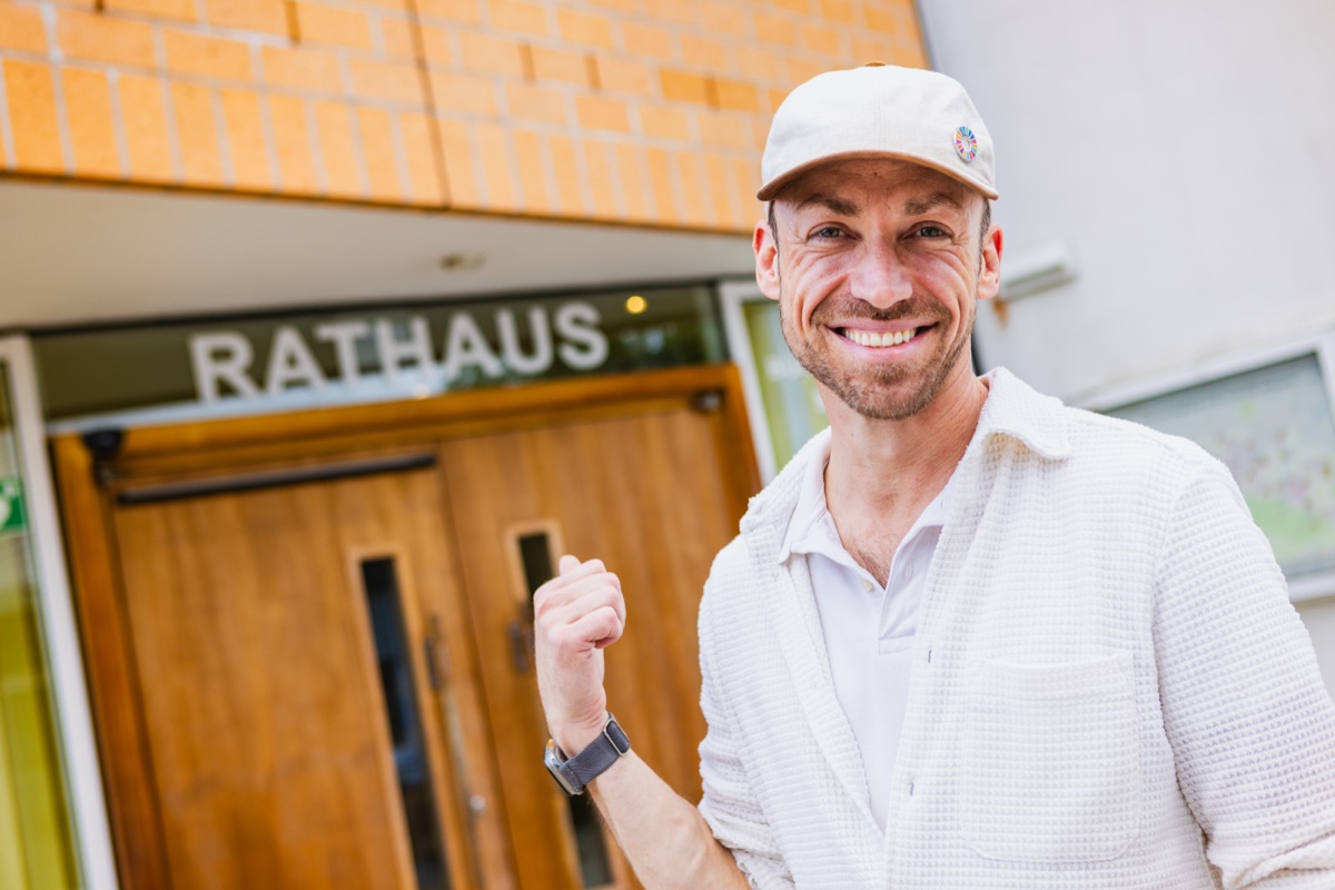 Roman Schladebusch mit heller Kappe vor der Eingangstür des Wennigser Rathauses, lachend, die Faust erhoben